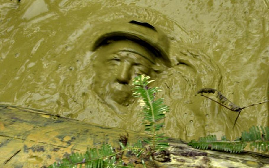 A Marine&#39;s face emerges from the muddy water of the "pit &#39;n&#39; pond" obstacle.