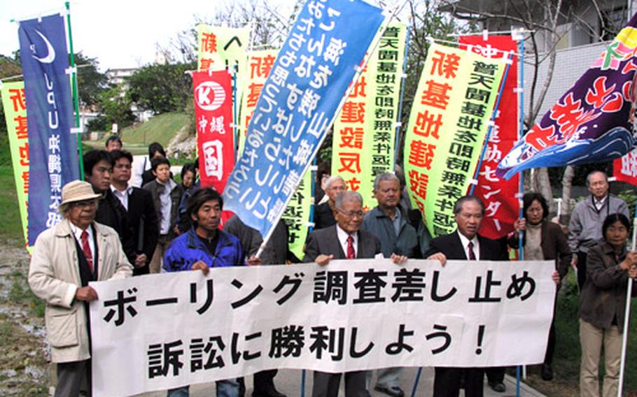 Opponents of the Marine air station planned for the waters off northeast Okinawa rally in front of the Naha District Courthouse Tuesday after opening arguments in a suit they filed against the Japanese government. The banner reads: "Win the lawsuit to suspend the drilling survey."