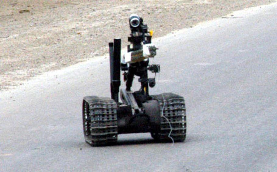 A small, tracked robot is maneuvered toward a roadside bomb by 766th Ordnance Company officials. An explosive ordnance disposal team destroyed the device, a hollowed-out log filled with artillery wires.