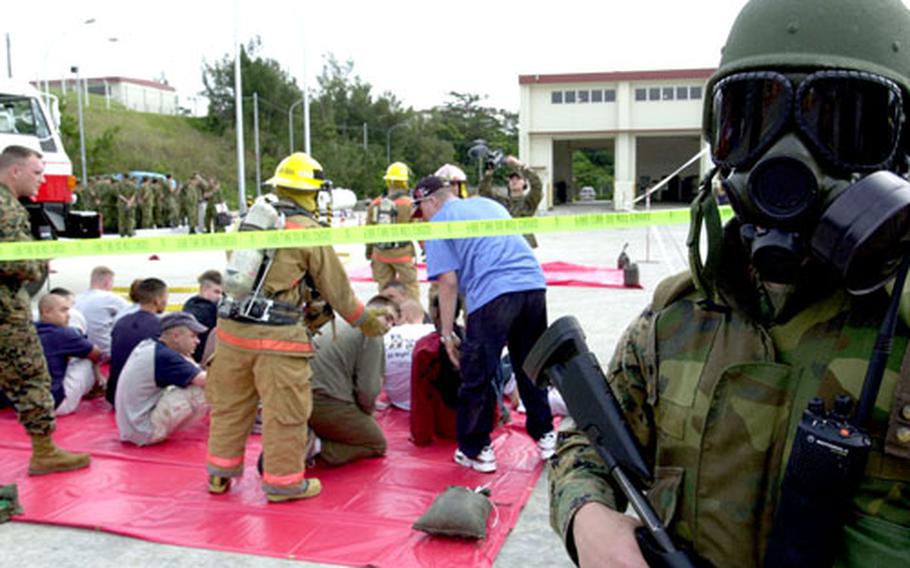 A Marine has donned his gas mask while standing guard outside the perimeter where a mock dirty bomb detonated on Camp Schwab, Okinawa, during a mass-casualty drill Thursday. In the background are the “walking wounded” who were just decontaminated and waiting for medical personnel to escort them out for examination.
