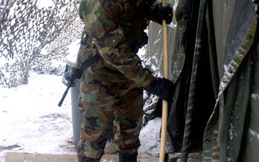 1st Lt. Jason Shin, Bravo Company platoon leader, 304th Signal Battalion, 1st Signal Brigade, sweeps the entrance of the mess tent after a snowfall during Reception, Staging, Onward Movement, and Integration.