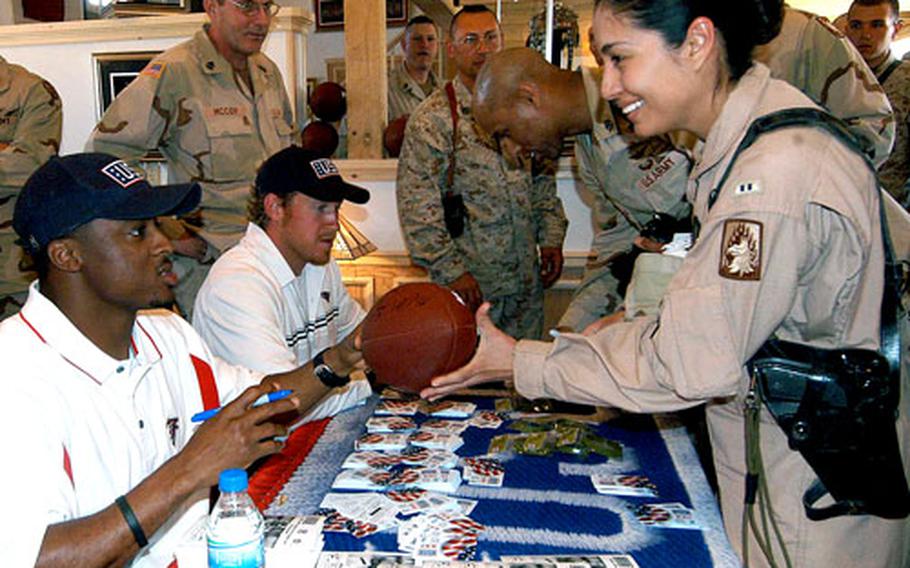 Chief Warrant Officer 2 Elvia Palumbo of the 3rd Battalion,158th Aviation Regiment out of Giebelstadt, Germany, has a football signed by Atlanta Falcons running back Warrick Dunn, left, as Larry Izzo of the New England Patriots signs autographs at center after the opening of the Pat Tillman USO Center at Bagram Air Base, Afghanistan.