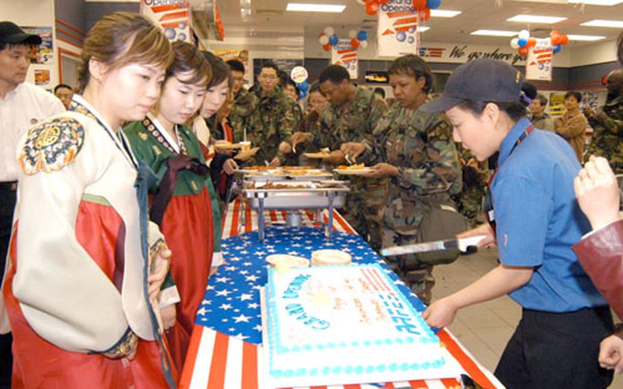 Korean women view a grand-opening sheet cake as soldiers in the background sample offerings during the grand reopening of newly revamped food court March 24 at Camp Carroll in Waegwan, South Korea.