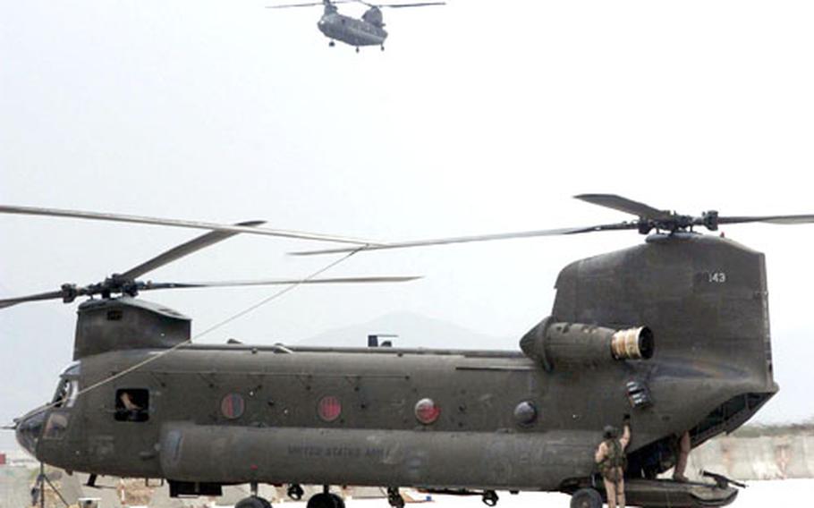 A CH-47 Chinook of Task Force Sabre comes in for a landing at Bagram Air Base, Afghanistan, as the crew of another Chinook prepares for the next mission.