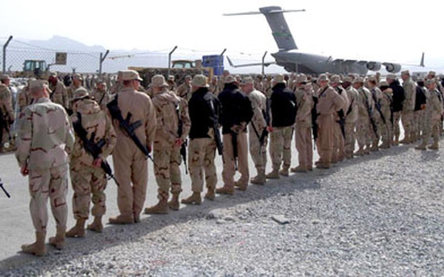 Servicemembers and civilians line the road to the Bagram Air Base flight line as they wait for the procession of Humvees carrying the coffins of the 18 victims of Wednesday’s helicopter crash near Ghazni, to a U.S. Air Force C-17, seen in the background.