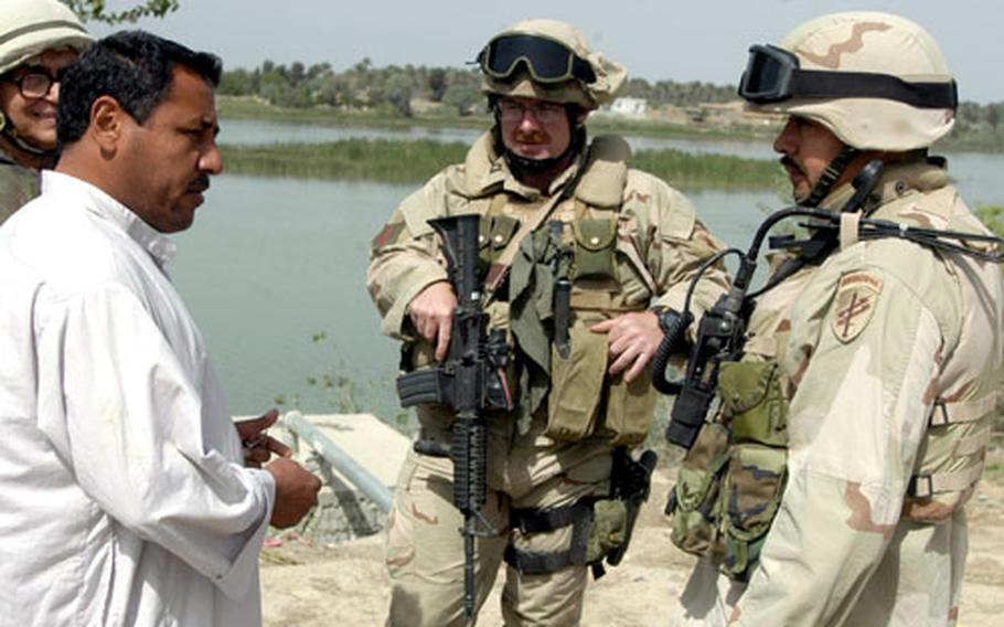 Capt. Andy McConnell, center, and Staff Sgt. Rene Ortiz, right, consult with an Iraqi contractor on a project that would bring water from the Tigris River, background, into the village of Bichigan, Iraq.