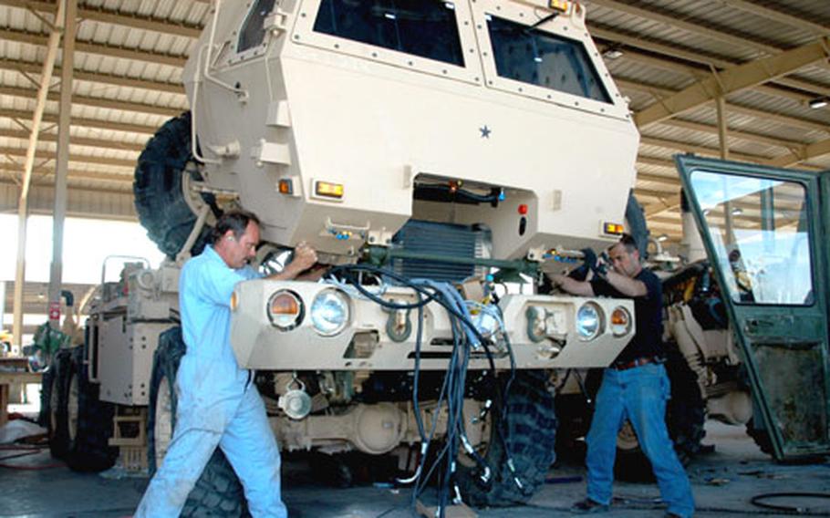 Pat Smith, left, and James Thorn, civilian contractors from the Norfolk Naval Shipyard in Virginia, guide the up-armored cab of a FMTV, or Family of Medium Tactical Vehicles, onto the frame at Camp Arifjan, Kuwait.