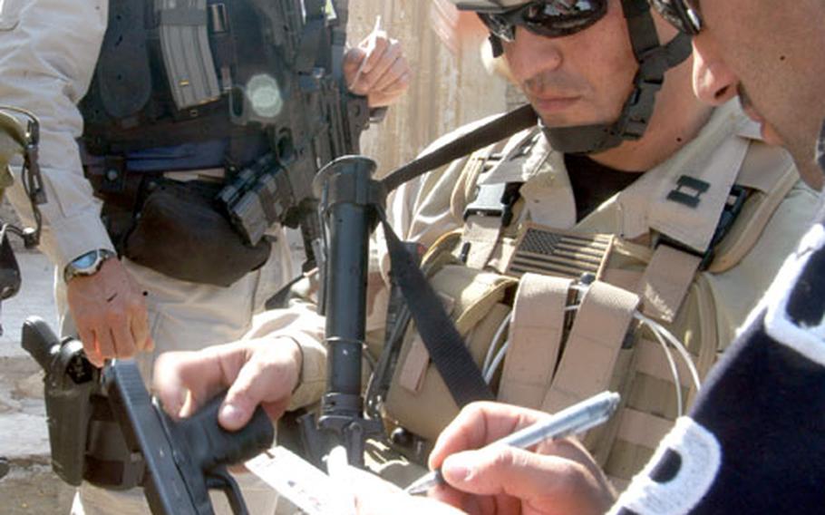 Capt. Thomas Venable, 36, a law enforcement advisor under the Joint Area Support Group in Baghdad, helps an Iraqi policeman record a handgun, confiscated Tuesday from a man who did not have the proper paperwork to carry the weapon.