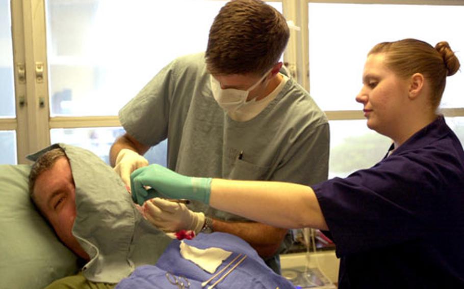 Lt. Cmdr. Eric Parlette, U.S. Naval Hospital Okinawa dermatologist, removes cancerous skin from behind 3rd Marine Division chaplain Capt. Robert Crossan’s ear with the help of Petty Officer 3rd Class Kari Riggs. Crossan has had problems with skin cancer for years; he said it was due to growing up in California and never wearing sunscreen.