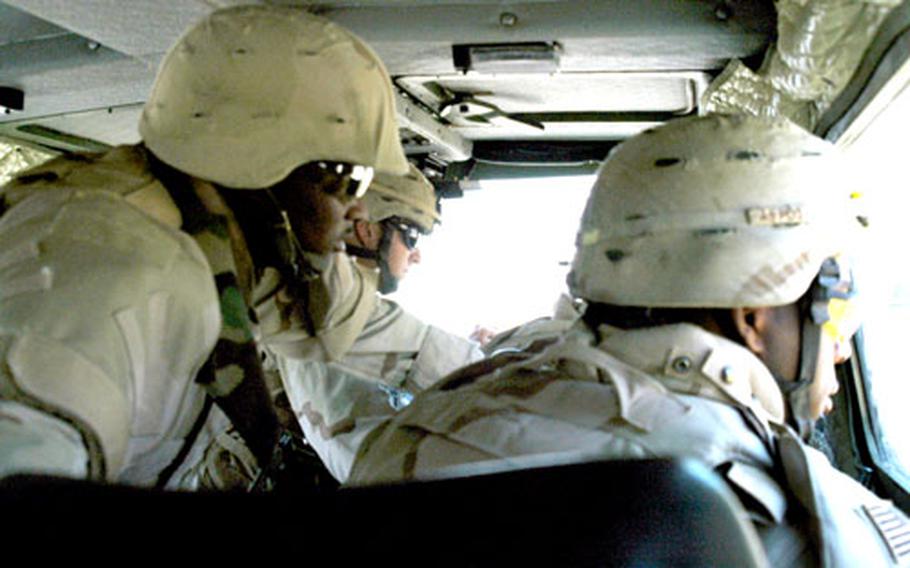 Sgts. Herman Peterson, left, Shane Reed, center, and Michael Lamb watch as Sgt. Jared Provost (not pictured) steers a mechanical arm to discover whether a cardboard box is hiding a bomb on a Baghdad boulevard. The box was empty, but earlier in the day, the crew discovered three improvised explosive devices.