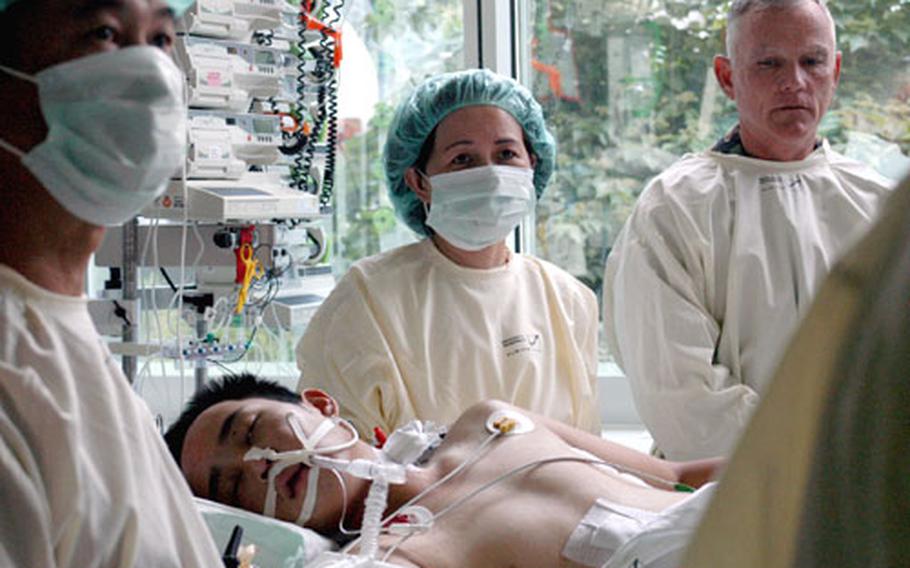 Elizabeth Lien Chu, center, and David Kim Wong, left, stand over their son, Sgt. Chang Wong of the 1st Squadron, 11th Armored Cavalry Regiment, while the recovering soldier receives a special grant of American citizenship Monday at a university hospital in Regensburg, Germany. Wong was sent to the hospital because its staff includes the foremost authorities in a new "external lung" that kept him alive after being wounded by a roadside bomb in Iraq. Col. Mike Davis, right, a former commander of Wong&#39;s unit, looks on during the ceremony.