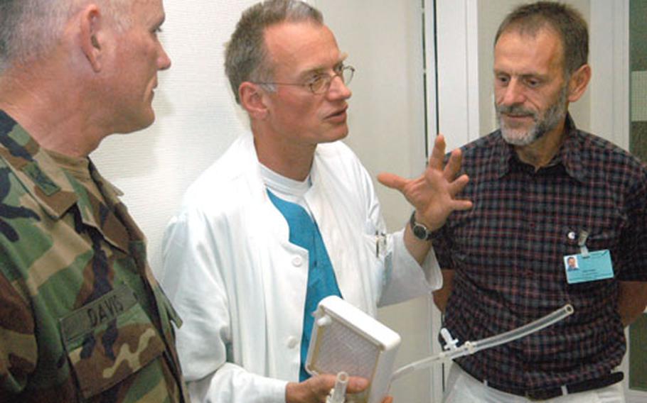 Novalung co-inventors Dr. Thomas Bein, center, and Philipp Alois, right, explain to Col. Mike Peters how the small box helps patients with disabled lungs keep oxygen in their blood.