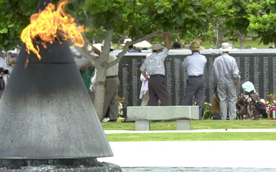 The Eternal Flame at Peace Prayer Park in Itoman burns as Okinawans look at panels containing names of those killed in the Battle of Okinawa.