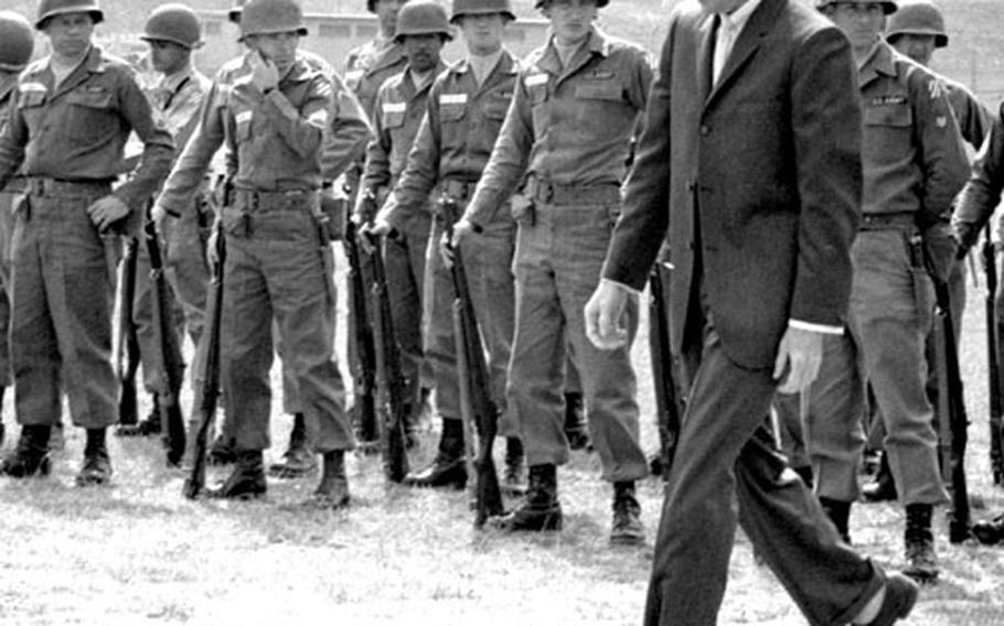 Soldiers watch as Audie Murphy walks across the set.