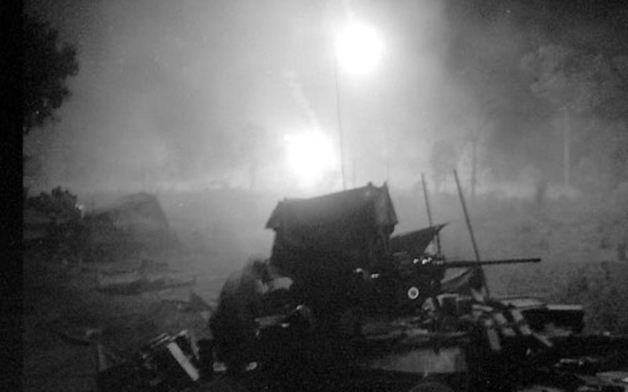 Armored vehicles are silhouetted against the light from flares during a night firefight.