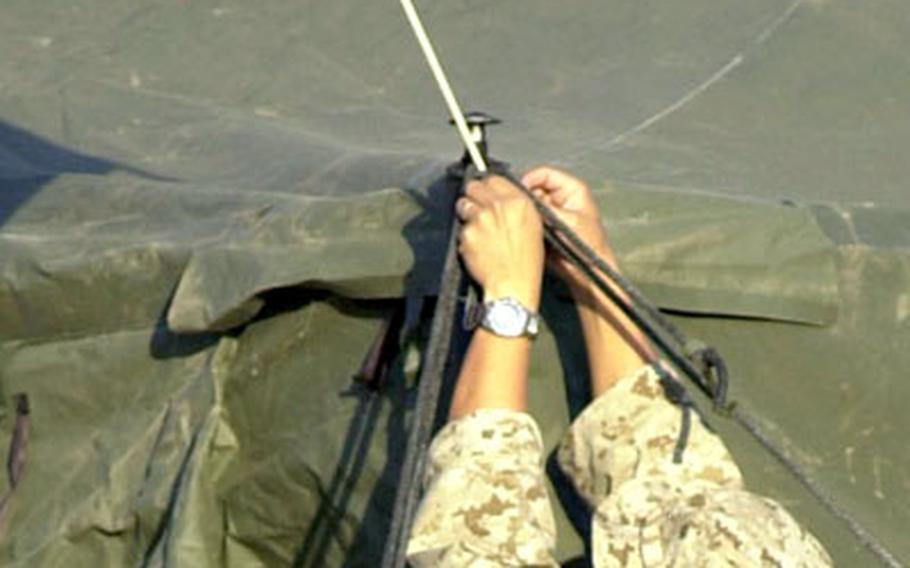 Capt. Danny S. Chung, 3rd Marine Logistics Group spokesman, puts the finishing touches on the tent he shares by placing a U.S. flag at the entrance.