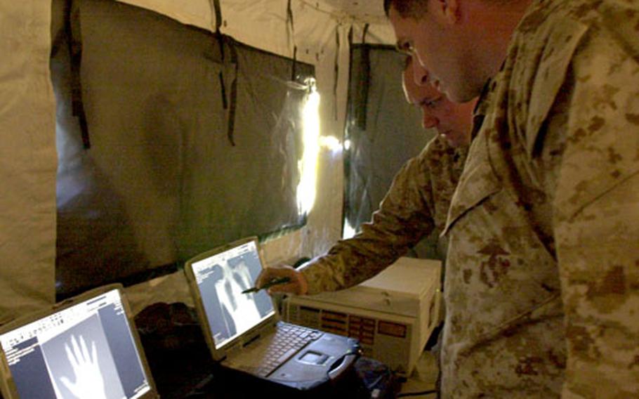 Lt. Cmdr. Fred Reed, a family physician with Bravo Surgical Company, and Petty Officer 2nd Class Doyle McClellan, an X-ray technician with the unit, look at the chest X-ray of Muhammad Siab Khan.