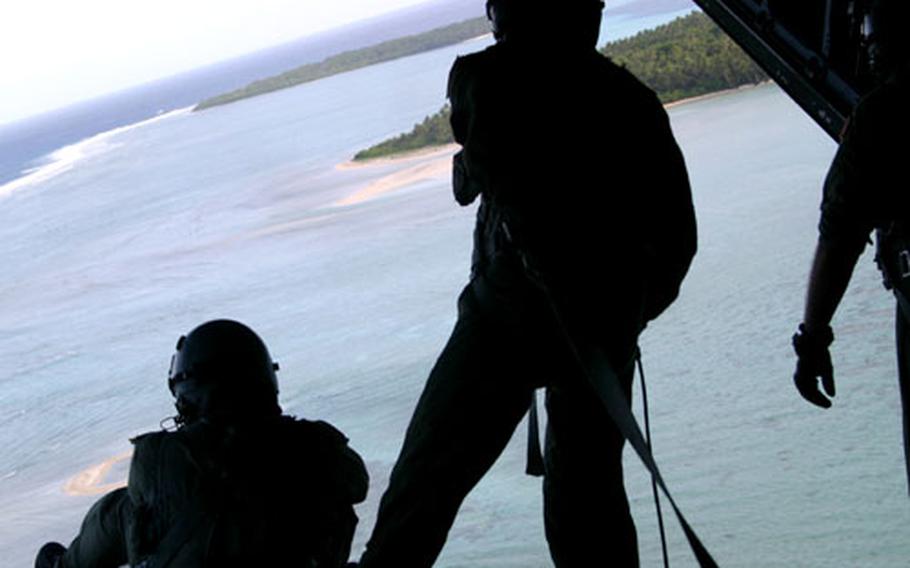 Tech. Sgt. Walter Fujioka, left, and Master Sgt. Kevin Saquilan watch islanders retrieve the boxes they just dropped out of their C-130 during the 2005 Christmas Drop out of Andersen Air Force Base, Guam.