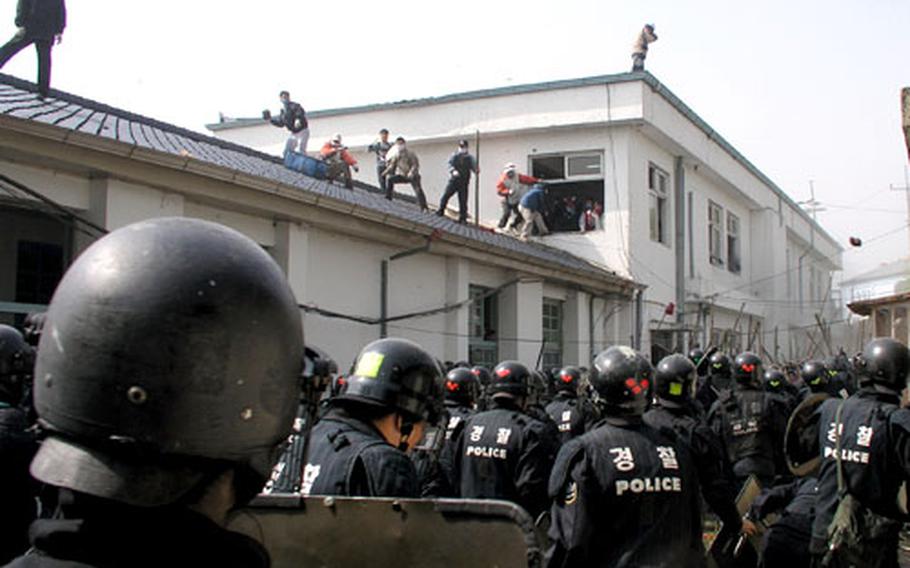 South Korean riot police sweep behind the Daechu-ri Elementary School on May 4 during an operation to oust barricaded protesters from the school grounds. Protesters on roof pelted police with a variety of objects, including furniture and window frames. Once police had gained control of the building, government work crews tore it down.