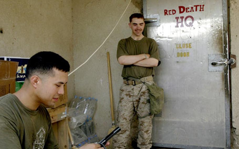 Marine Sgt. Dean Long, left, and Lance Cpl. Noah Welter take a break at Operation Post Omar. The heavy refrigerator door beside Welter was the entryway to an Iraqi morgue cooler, but now serves as the door to the Marines’ living area.