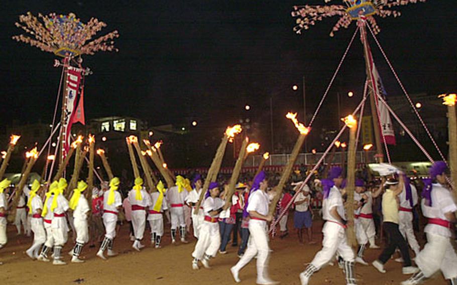 Local performers and audience members circle around two poles during a flag bearer competition and wild procession of torchlight.