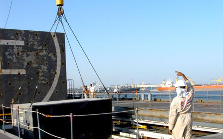 A civilian contractor motions last week as a crane lifts a container into the USNS Mendonca at the port.