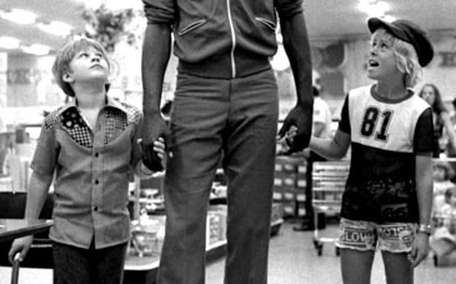Moses Malone, the 6-10 Houston Rockets basketball star, towers over Roger Hudnell, left, and Phinney Barnes during a visit to the AAFES store at Wiesbaden, Germany.