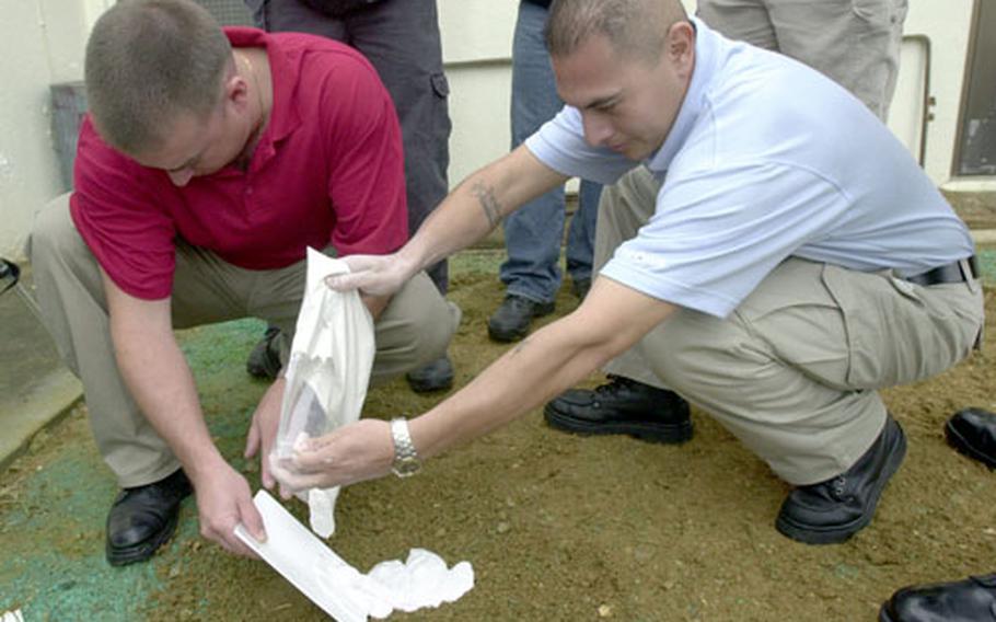 Petty Officer 1st Class Tony Colosi directs the flow of the dental modeling plaster into a footprint as Petty Officer 1st Class Armando Covarrubias pours the plaster into the impression.