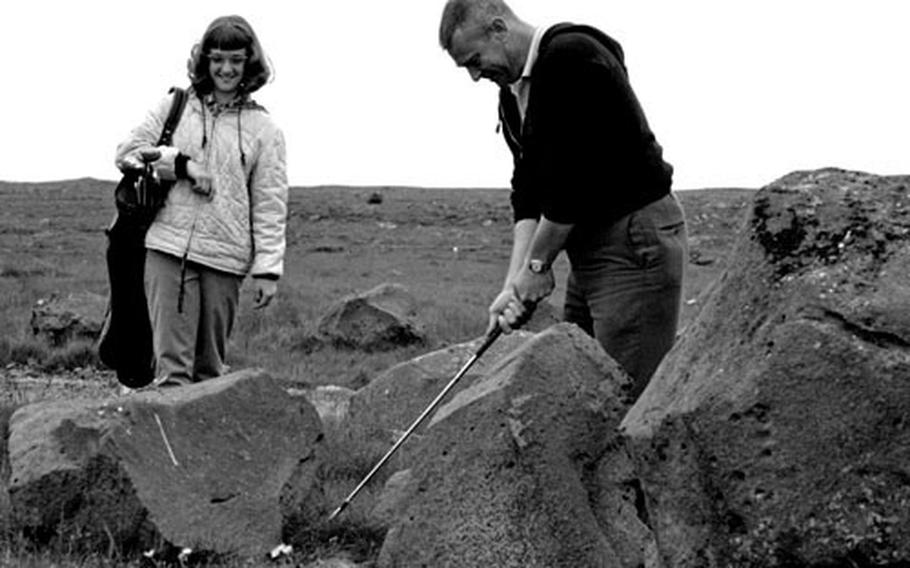 Caddy Sandy Emmert waits as CPO John E. Emert chips out from between some of Iceland&#39;s volcanic boulders.