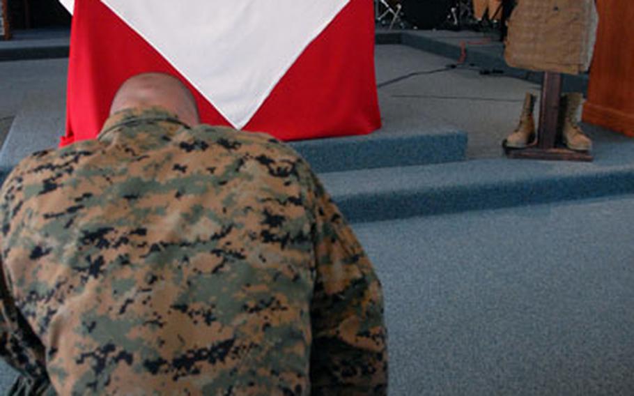 A Marine kneels in front of a photograph of Cpl. Jennifer Parcell, a Marine with 3rd Marine Logistics Group who was killed in Iraq last week. At the Camp Foster memorial service Tuesday, her comrades described her as a "fire cracker" and an "extraodinary Marine." A photo of Parcell with friends is on the projector screen in the background.