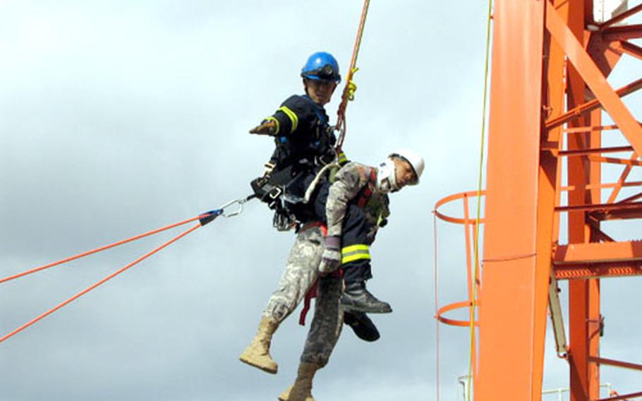 Firefighter Diaki Kawabata motions for his crew to begin to lower him down from a communications tower on Camp Foster during tower rescue training Thursday. Army Sgt. David Gonzalez. Gonzalez organized the drill and played the part of one of two "victims" during Friday&#39;s scenario.