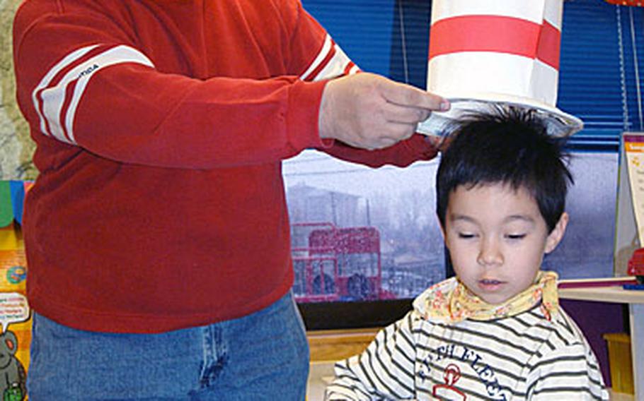 Parent-volunteer Kevin King helps his five-year-old Alex try on newly-constructed "Cat in the Hat" headwear during the "Read Across America Day" activities in Ruth Ann Emery&#39;s kindergarten classroom at Seoul American Elementary School, Friday.