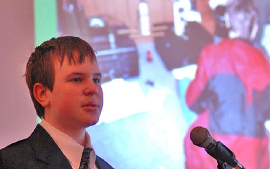 Michael Rynders, an eighth-grader at Landstuhl Middle School in Germany, answers questions after his oral presentation on a test of the accuracy of radiation as a thickness-measuring tool at DODDS European Junior Science and Humanities Symposium. On the screen behind him is a photo of Michael doing the test.