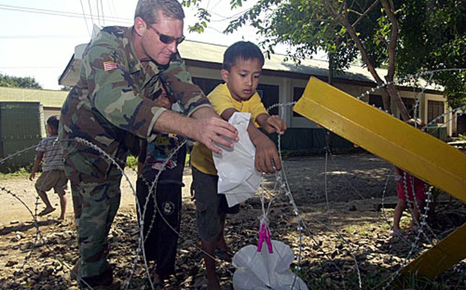 U.S. Army Master Sgt. Dan Raines of the 19th Special Forces Group helps local children untangle their handmade parachute toys from a concertina-wire fence at the U.S. compound on Jolo Island, Philippines.