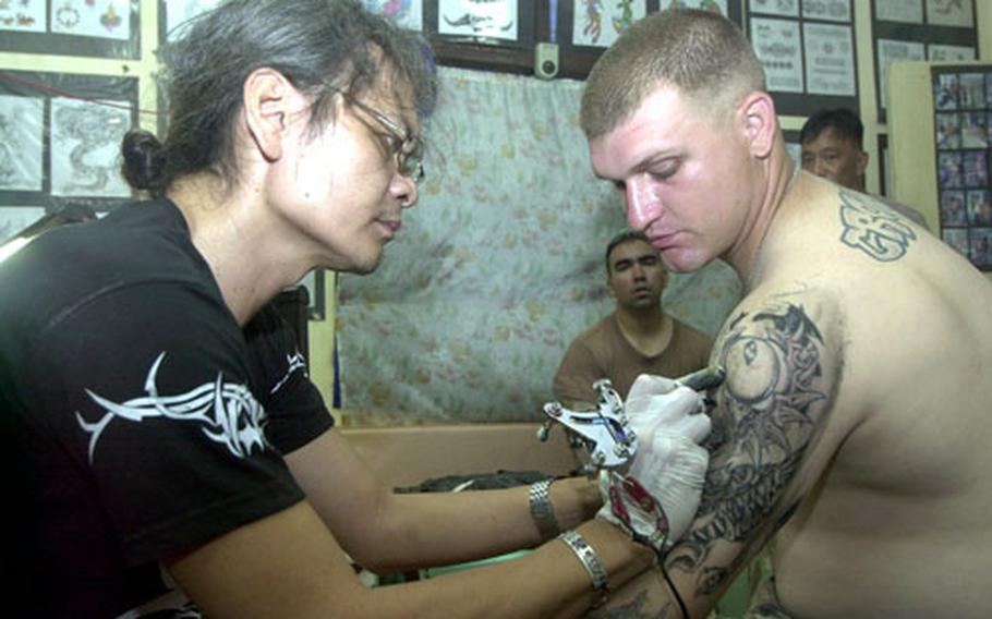 Army Sgt. Clifton Crowder of the 1st Battalion, 21st Brigade, 25th Infantry Division watches as tattoo artist Jess Santos works on his arm at Camp Bautista on Jolo Island, Philippines.