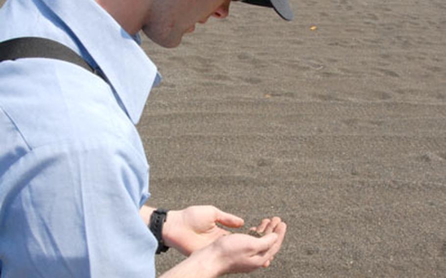 Seaman Joshua Langland holds a fistful of sand from Invasion Beach on Iwo Jima, where the Americans started their massive amphibious assualt on the island. Langland&#39;s grandfather was a part of that attack.