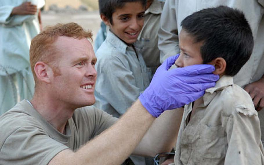 Spc. Justin Forth, 3rd Platoon, Company C, 1st Battalion, 32nd Infantry Regiment, 10th Mountain Division, gives some first aid to a local boy who showed up at the Fire Base Florida gate with cut on his cheek.