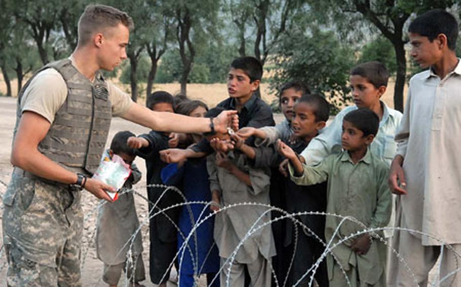 Pfc. John McConnell, 3rd Platoon, Company C, 1st Battalion, 32nd Infantry Regiment, 10th Mountain Division, hands out pumpkin seeds to local children at the gate of Fire Base Florida. The soldiers of 3rd Platoon have mostly a good working relationship with the locals along their stretch of the Pech valley.