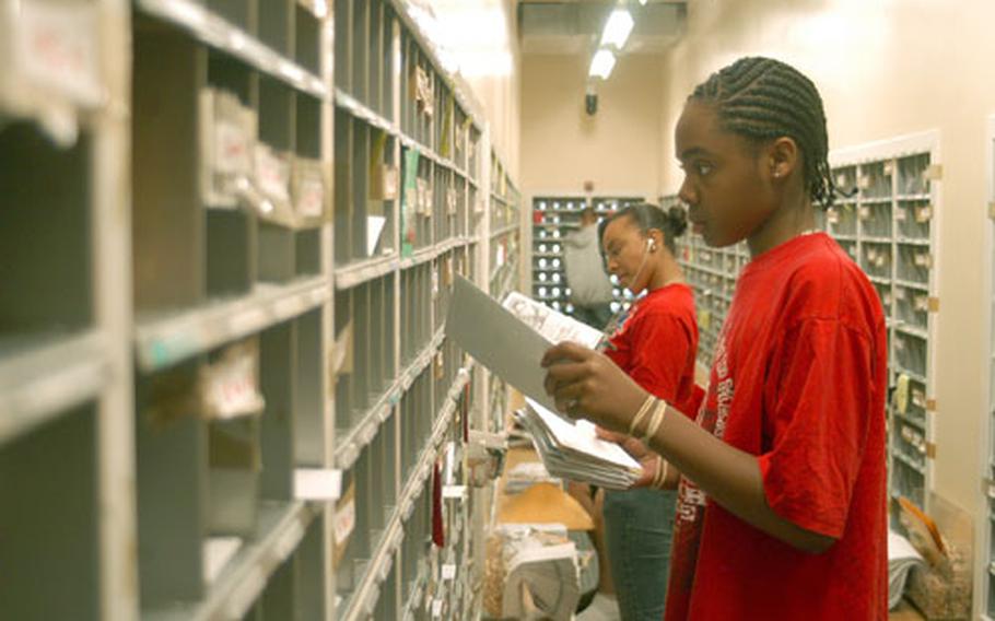 Malcolm Jennings, 14, and 15-year-old Devan Drayton (background) sort through mail inside RAF Mildenhall&#39;s Post Office. Both are working full-time jobs as part of the U.K.-wide Summer Hire program.