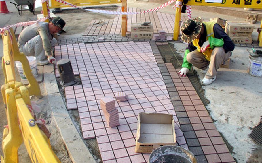 At the Anjung-ri commercial strip outside Camp Humphreys in South Korea, Monday, workers lay tile for new sidewalks. Businesses in the district cater largely to U.S. servicemembers.