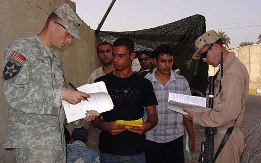 Army Spc. Paris Taylor (left), assigned to the 2nd Cavalry Division&#39;s 2nd Battalion, 12th Infantry Regiment, and Air Force Staff Sgt. J. Osborne (right) check the paperwork of Iraqi police recruits.