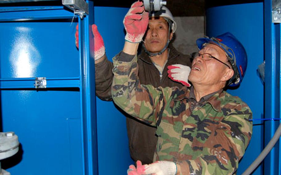 Plumbers Yu Chang-myong, foreground, and Mun Heung-min install gaskets between the pipes separating the two water tanks of the new Hannam Village water filtration system on Thursday.