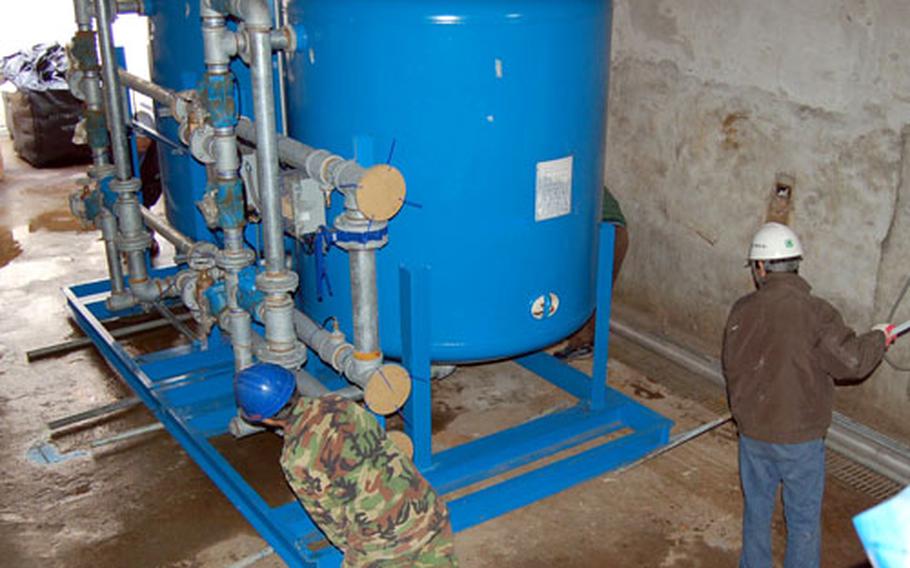 Plumbers push the water tanks of the new Hannam Village water filtration system into place on Thursday.