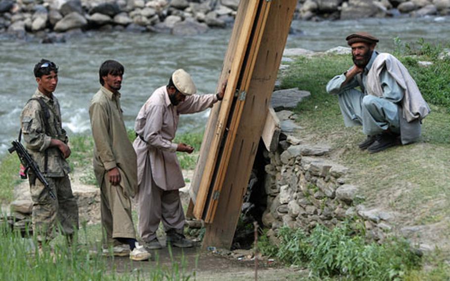 An Afghan border policeman and several men gather around a man with a stand that sells cigarettes, gum and other small items.