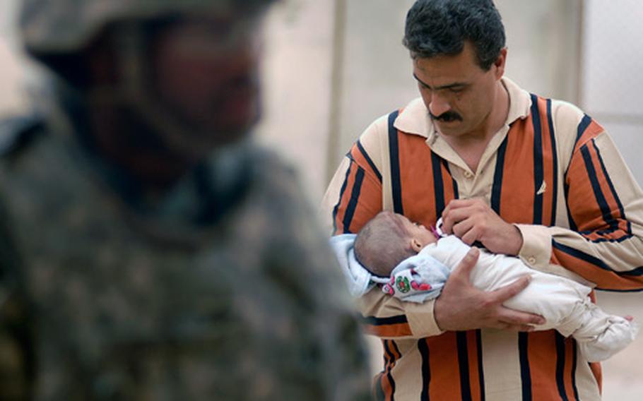 A soldier leads Abdul Kadum Hamdi, carrying his daughter Marian, to the medical clinic during preparation for a medical evacuation.