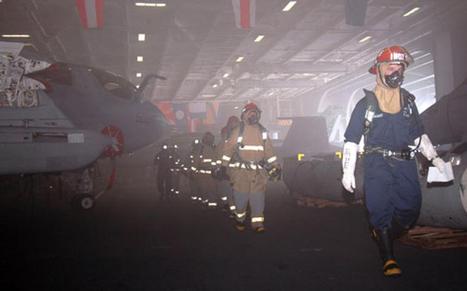 Fire Team Leader,Machinery Repairman 2nd Class William Neault, guides his team into Hangar Bay 3. The comprehensive firefighting effort extinguished all fires while limiting shipboard damage and preventing any serious injuries for the crew.