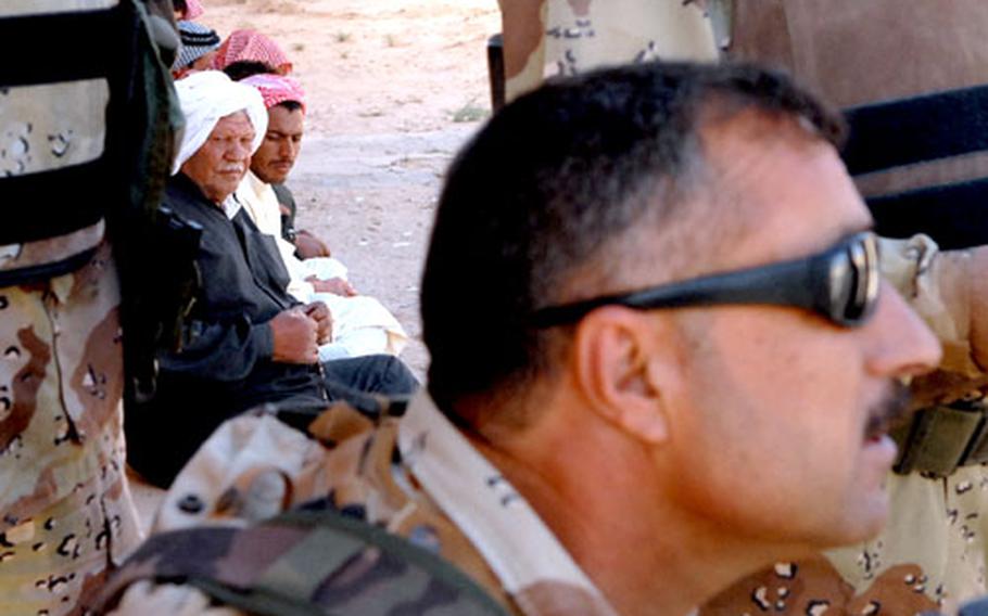 Residents of Marzuga Al Marghab, Iraq, who have already been questioned watch Iraqi soldiers question their neighbors.