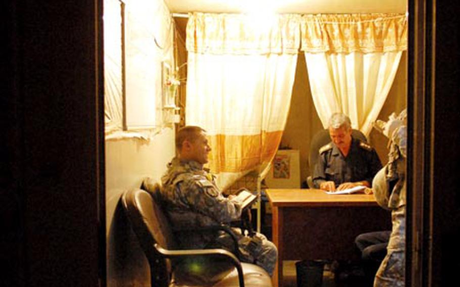 Staff Sgt. Eugene Fosmire, a squad leader in the 116th Military Police Company (left), jokes with an Iraqi Police chief while checking in on his Afghani, Iraq, station late Sunday night. The “station” is a collection of premade housing units similar to an American trailer park.