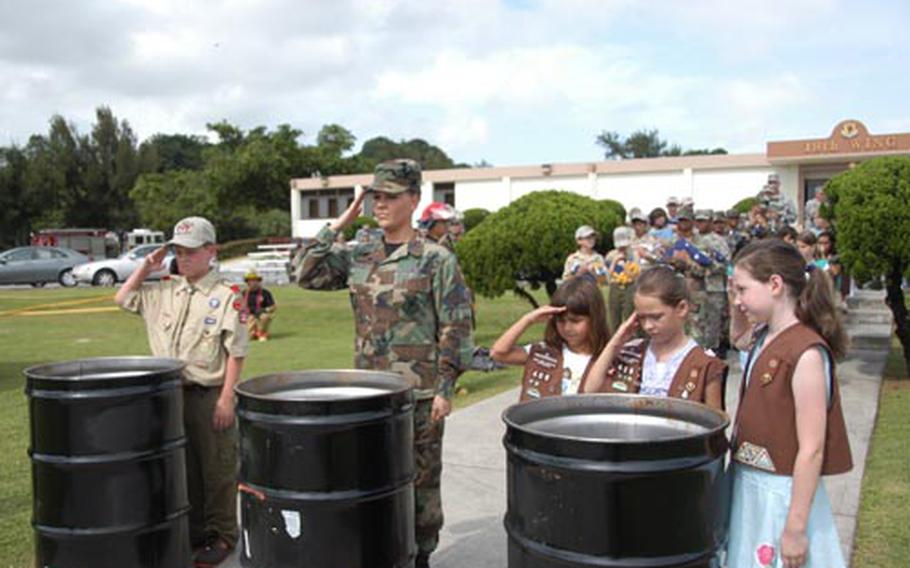 A group of scouts and an airman salute after placing old flags in a bin to be retired.