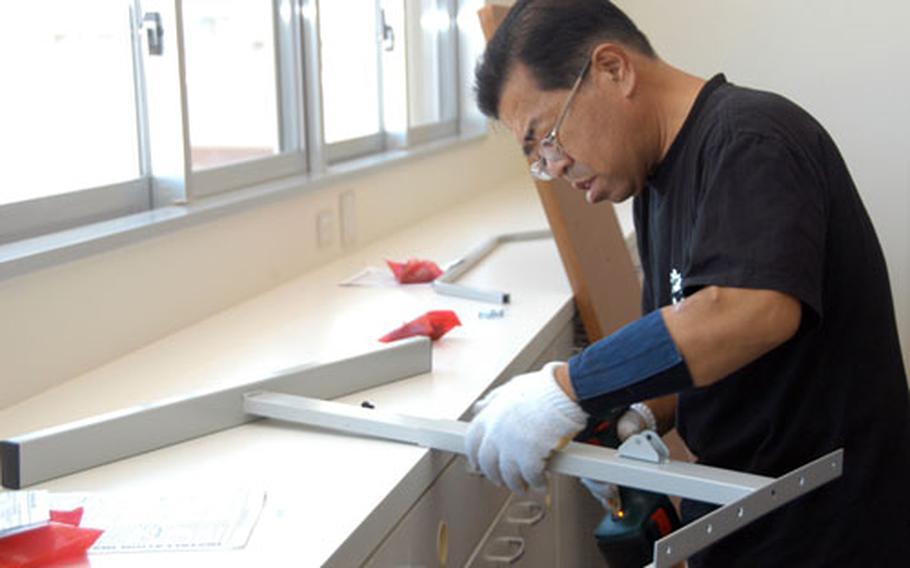 Masahide Tamaki, of the maintenance crew at Ryukyu Middle School, assembles parts for a desk.